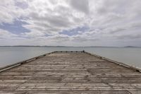 wooden dock overlooking sea with clouds in background and mountains in distance, at the end of dock