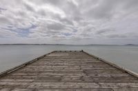 wooden dock overlooking sea with clouds in background and mountains in distance, at the end of dock