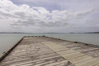 wooden dock extending into open water with mountains in the background under a cloudy sky and white clouds