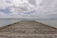 an old wooden dock over looking water on a cloudy day during the day with white clouds