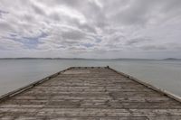 an old wooden dock over looking water on a cloudy day during the day with white clouds