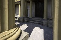 columns are seen outside a stone building near some steps and an entranceway with a wooden door