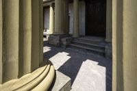 columns are seen outside a stone building near some steps and an entranceway with a wooden door