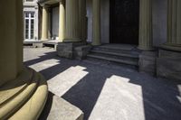 columns are seen outside a stone building near some steps and an entranceway with a wooden door