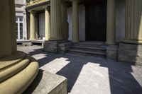 columns are seen outside a stone building near some steps and an entranceway with a wooden door