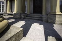 columns are seen outside a stone building near some steps and an entranceway with a wooden door