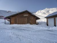 a wooden building with some skis on top and snowy mountains in the background on a cold day