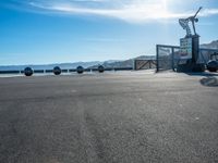 the parking area is empty with people standing and sitting around it's side near an ocean