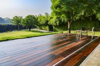 wooden patio with chair and table overlooking a lush green field outdoors setting with pool and spa