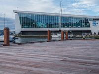 a boardwalk next to boats and a glass building with large windows on the sides and windows on the side