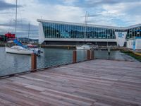 a boardwalk next to boats and a glass building with large windows on the sides and windows on the side