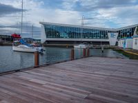 a boardwalk next to boats and a glass building with large windows on the sides and windows on the side