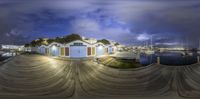 the view from the fish eye lens shows some boats and a hill at night in a small harbor