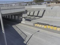 a yellow and black trashcan sitting on the side of an overpass next to concrete columns