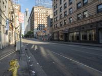 a yellow fire hydrant in an empty city street with tall buildings on the other side