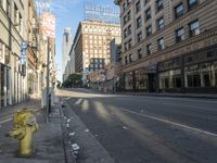 a yellow fire hydrant in an empty city street with tall buildings on the other side