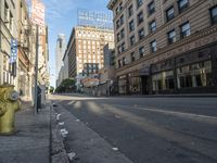 a yellow fire hydrant in an empty city street with tall buildings on the other side