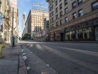 a yellow fire hydrant in an empty city street with tall buildings on the other side