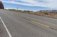 a single yellow painted line on a highway near mountains and rocks and boulders that look like they are melting