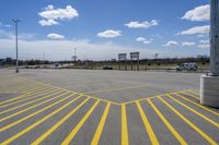 a parking lot with lots of yellow lines painted on it in front of a blue and white sky with clouds