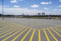 a parking lot with lots of yellow lines painted on it in front of a blue and white sky with clouds