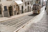 the yellow tram is on tracks running through an old narrow alleyway with white buildings