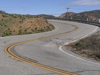 the yellow double striped road is winding into the distance, with a bridge in the background