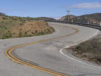 the yellow double striped road is winding into the distance, with a bridge in the background