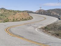 the yellow double striped road is winding into the distance, with a bridge in the background