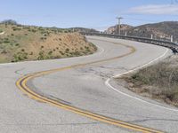 the yellow double striped road is winding into the distance, with a bridge in the background