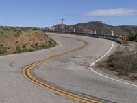 the yellow double striped road is winding into the distance, with a bridge in the background