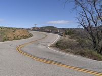 the yellow double striped road is winding into the distance, with a bridge in the background