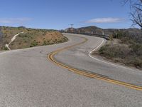 the yellow double striped road is winding into the distance, with a bridge in the background