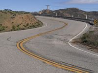 the yellow double striped road is winding into the distance, with a bridge in the background