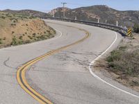 the yellow double striped road is winding into the distance, with a bridge in the background