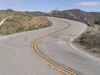 the yellow double striped road is winding into the distance, with a bridge in the background