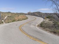 the yellow double striped road is winding into the distance, with a bridge in the background