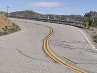 the yellow double striped road is winding into the distance, with a bridge in the background