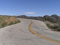 the yellow double striped road is winding into the distance, with a bridge in the background