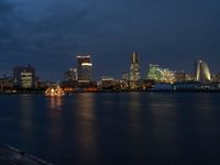 a city skyline at night lit up with bright lights reflecting in the water and a boat coming toward it