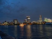 a city skyline at night lit up with bright lights reflecting in the water and a boat coming toward it