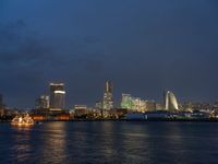 a city skyline at night lit up with bright lights reflecting in the water and a boat coming toward it