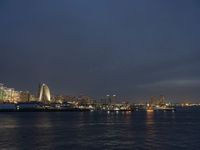 a city skyline at night lit up with bright lights reflecting in the water and a boat coming toward it