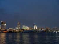 a city skyline at night lit up with bright lights reflecting in the water and a boat coming toward it