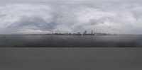an empty beach surrounded by water and clouds as the city skylines stand beyond a body of water