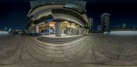 a spherical fisheye view of a store with stairs and clock tower at night in the city