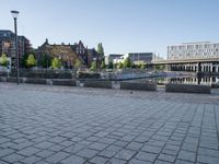 a young boy running across a brick paved sidewalk next to the water and a city