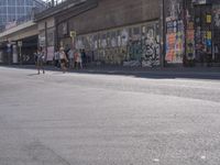 young people are riding skateboards down the city street in front of a graffiti covered wall