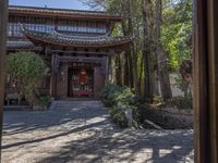 an asian building is surrounded by trees and stones in front of it, the stone flooring is also gray