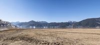 the grass is brown in color with many mountains in the back ground and snow covered mountains, blue sky, and clear water